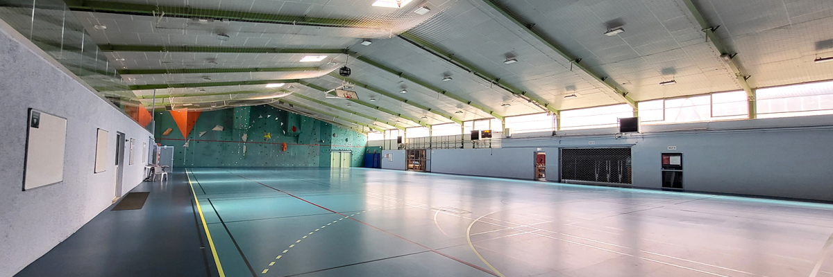 Salle de sport avec paniers de basket, murs d'escalade et éclairage.