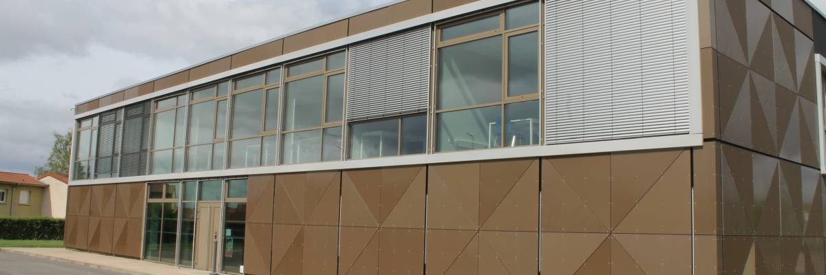 Bâtiment moderne avec façade en verre et panneaux métalliques, situé le long d'une route.