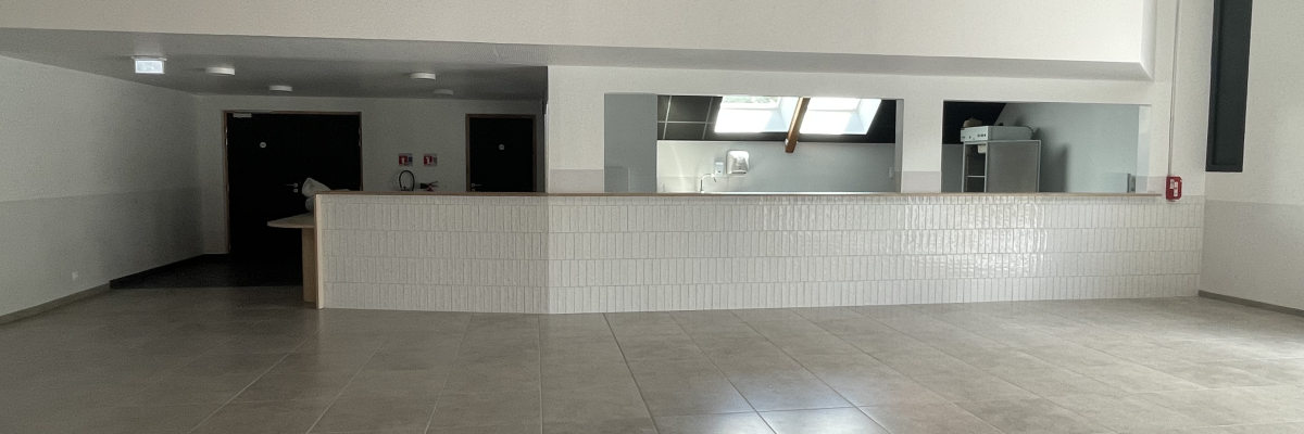 Salle vide avec comptoir, sol carrelé, portes et équipements muraux.