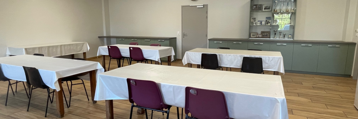 Salle avec tables, chaises, nappes, horloge, armoire et comptoir.