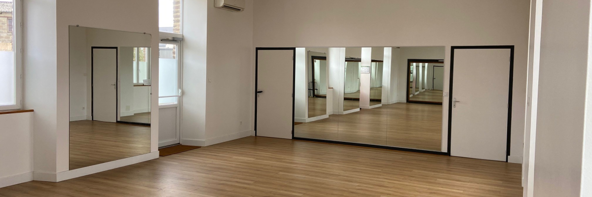Salle vide avec parquet, murs blancs, portes vitrées et climatisation au plafond.
