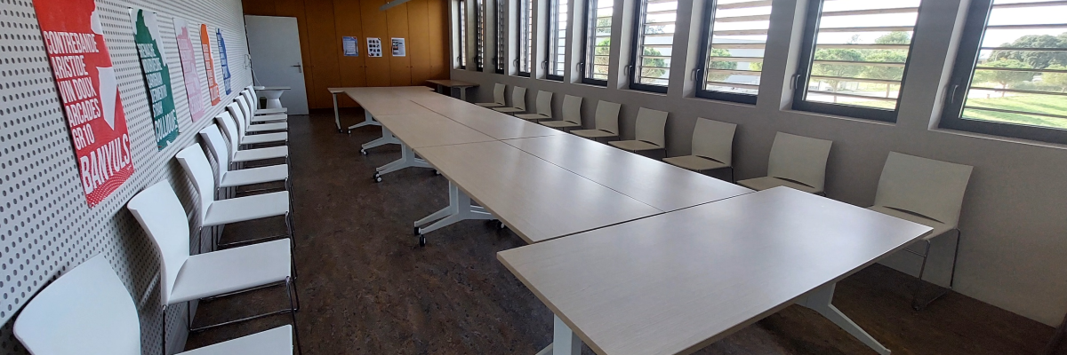 "Salle avec longues tables, chaises, fenêtres et affichages muraux."