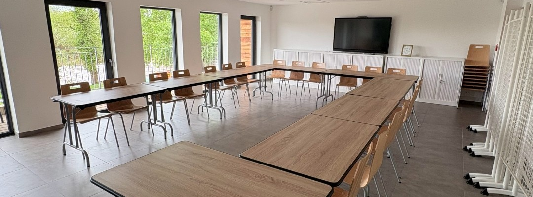 Salle avec tables, chaises, écran, climatiseur et rideaux.
