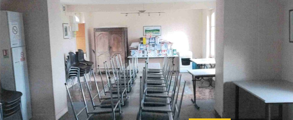 Salle de classe avec tables, chaises, table de professeur, ordinateur, étagères et extinction.