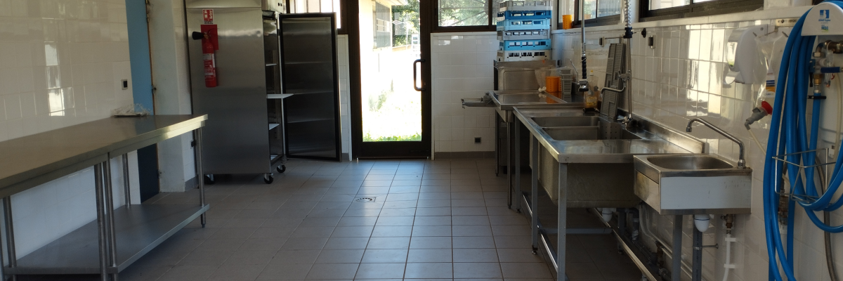 Cuisine équipée avec plans de travail, évier, lave-vaisselle, frigo, chariot et tuyaux.