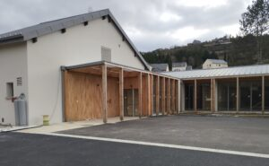 Bâtiment avec portes en bois et fenêtres, parking et montagne à l'arrière-plan.