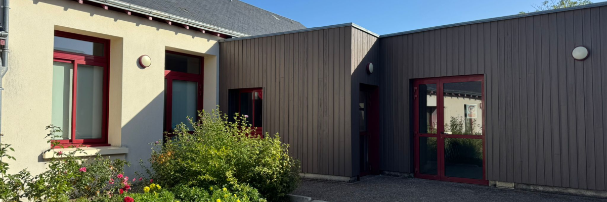 Bâtiment avec portes et fenêtres rouges, allée de gravier, plantes et pot de fleurs.