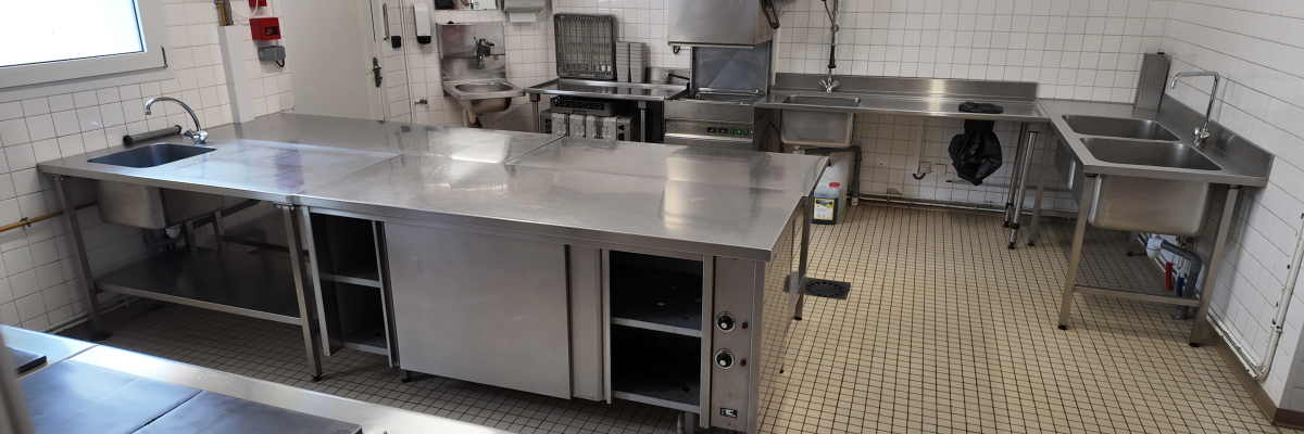 Cuisine avec plans de travail en acier inoxydable, éviers, plaques de cuisson, étagères et armoires.