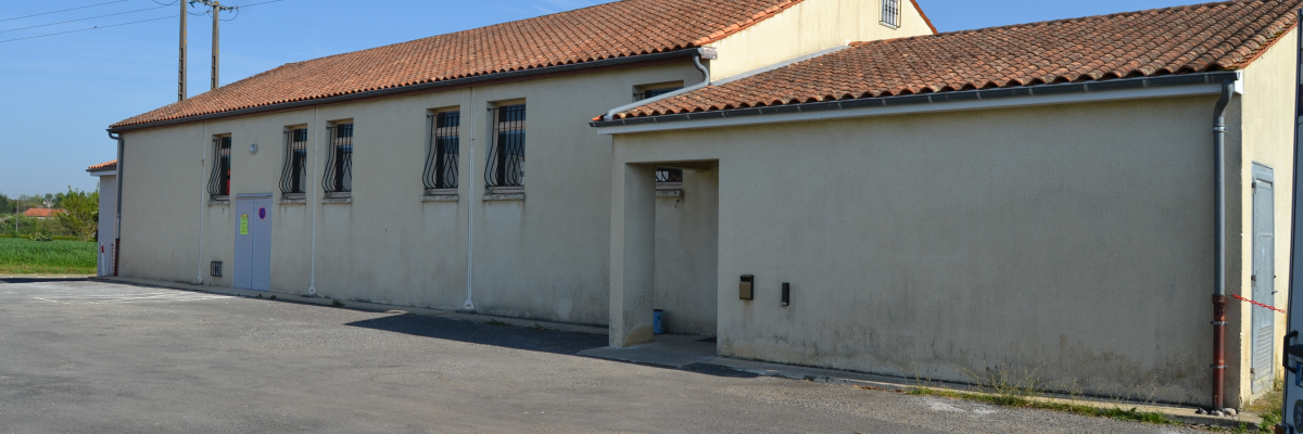 Bâtiment blanc, toit tuiles, fenêtres grillagées, porte métallique.