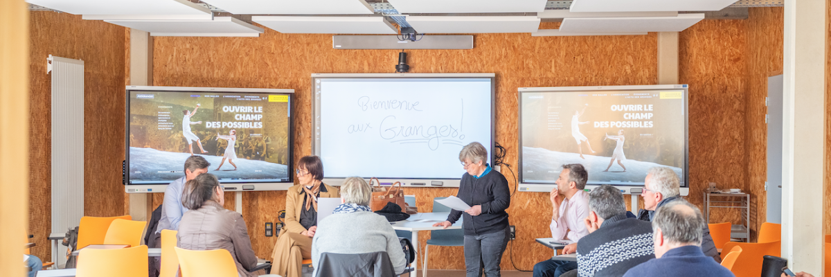 Salle de réunion avec écrans, table, chaises, paperboard.