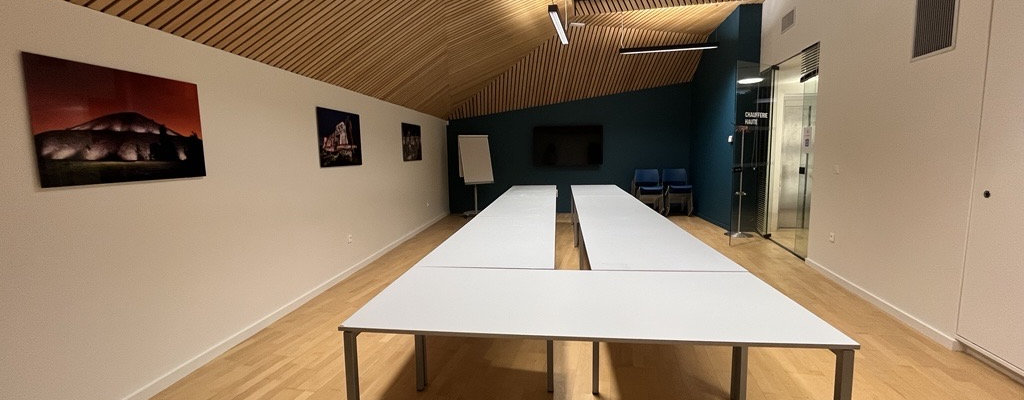 Salle avec tables, écran, tableau blanc, chaises, et peintures murales.