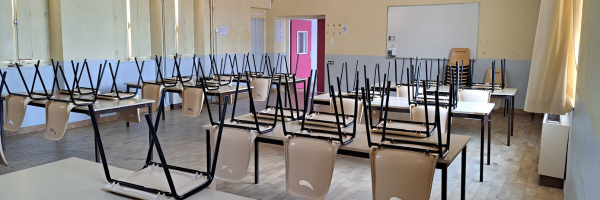 Salle de classe avec bureaux, chaises, tableau et porte rouge.