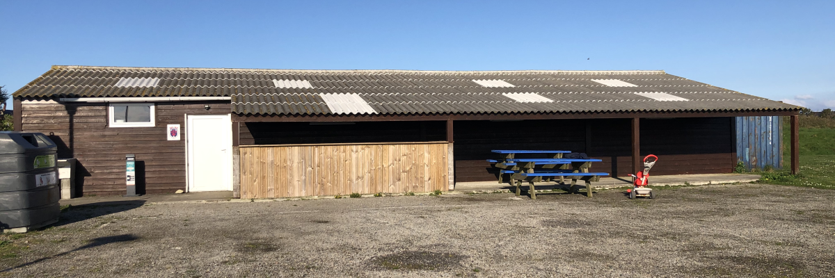 Bâtiment avec toit en tôle, porte en bois, table de pique-nique, banc et extincteur orange.