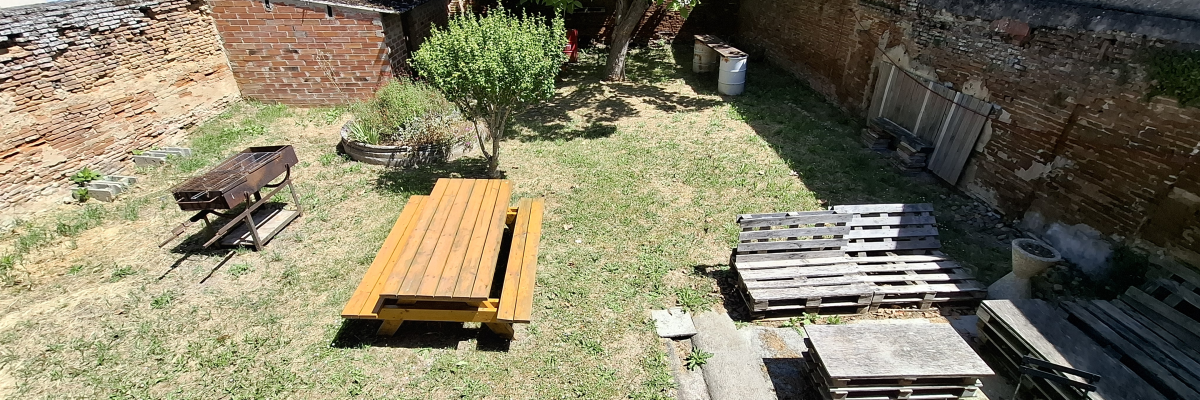 Cour avec banc, palettes, table ronde, arbre et murs en brique.