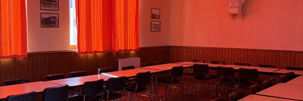 Salle avec tables, chaises, rideaux, affiches et parquet.