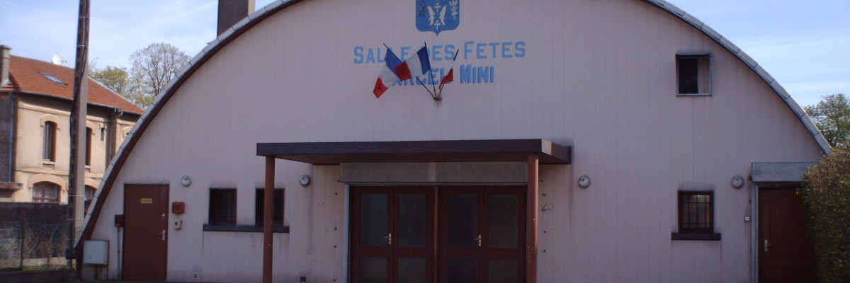 Bâtiment avec entrée centrale, portes latérales, blason et enseigne "Salle des fêtes mini".