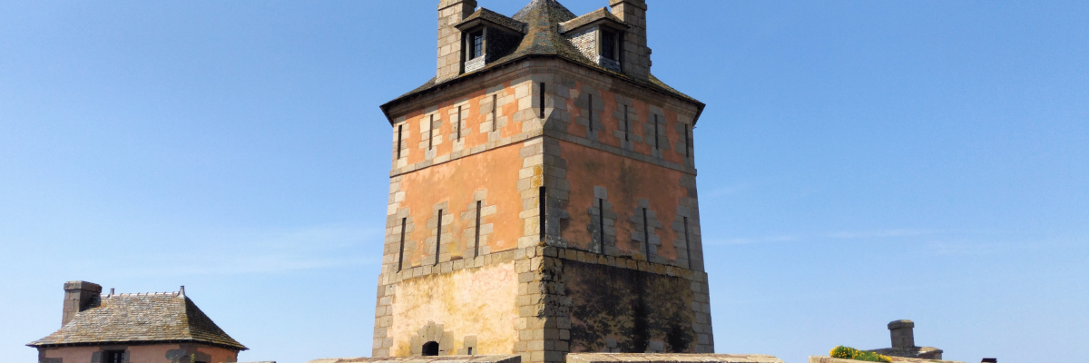 Tour de pierre avec toits pentus, entourée de remparts et de bâtiments annexes.