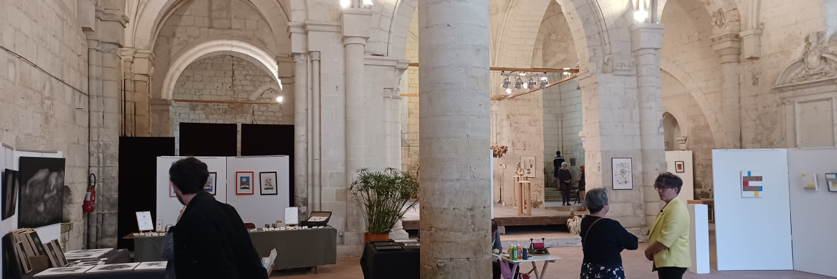 Salle voûtée avec colonnes, tables, chaises, présentoirs, œuvres d'art, et personnes.