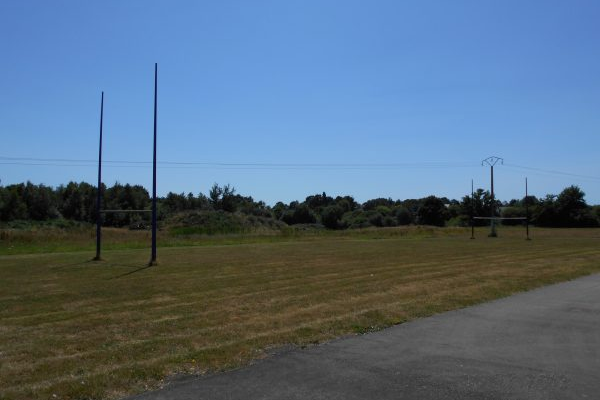 Terrain de sport avec but de volley-ball et panier de basket, piste autour.