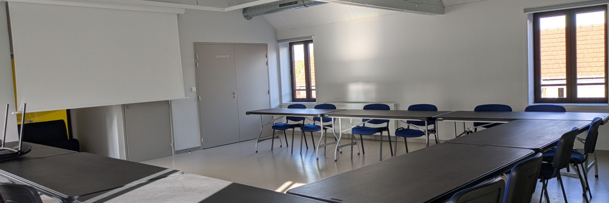 Salle avec tables, chaises, tableau blanc et porte.