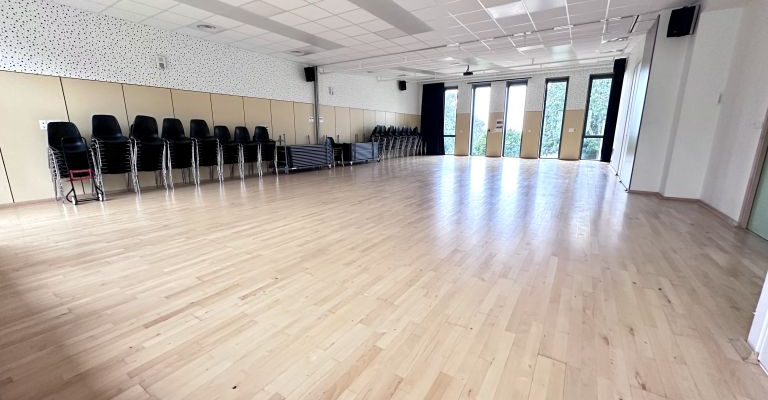 Salle avec parquet, chaises alignées, murs décorés, portes vitrées.