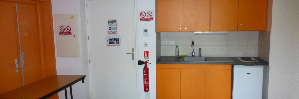 "Cuisine avec table, armoires, évier, plaque de cuisson, réfrigérateur et extincteur."