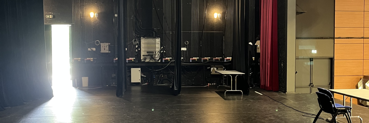 Salle avec scène, tables, chaises, écran, éclairages et rideaux.