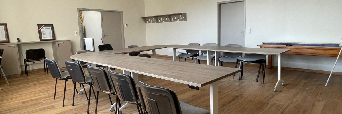 Salle de classe avec tables, chaises, tableau blanc et horloge.
