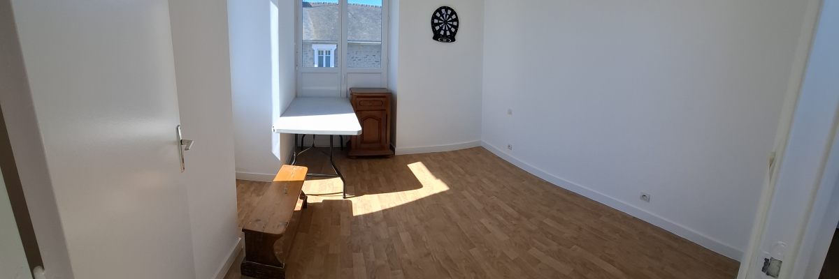 Pièce avec parquet, table, banc, fenêtre et porte. Mur blanc.