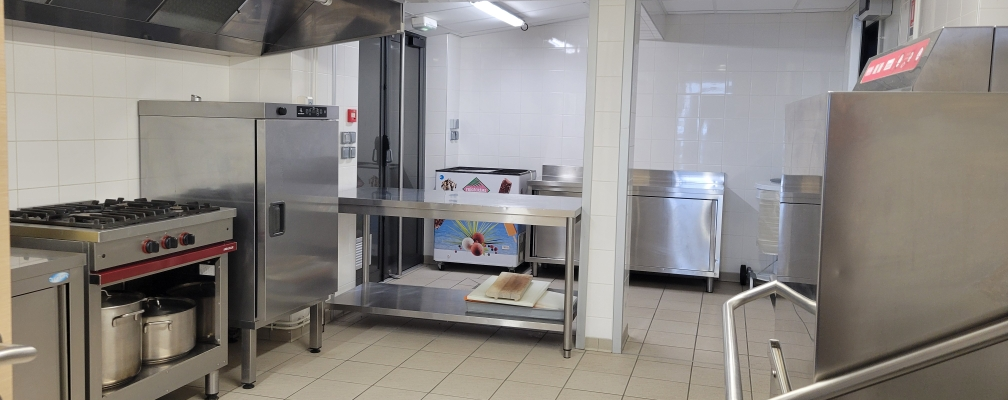 Cuisine professionnelle avec fourneaux, hottes, réfrigérateurs, étagères et plans de travail en acier inoxydable.