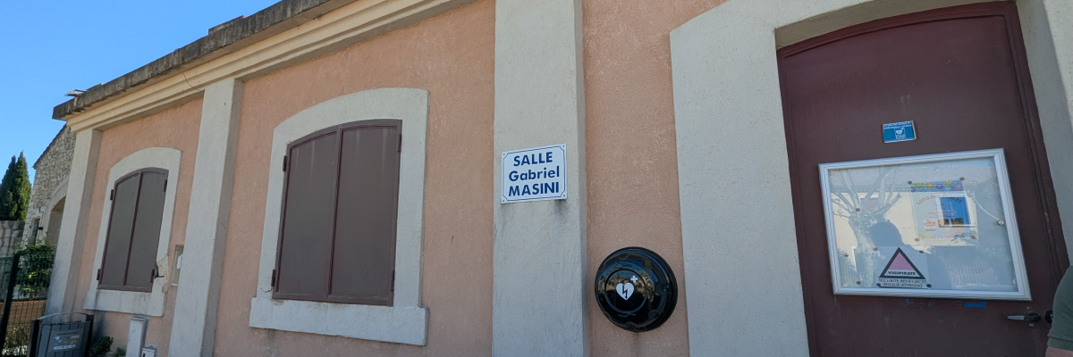Bâtiment avec fenêtres, porte, sonnette et panneau "Salle Gabriel Masini".