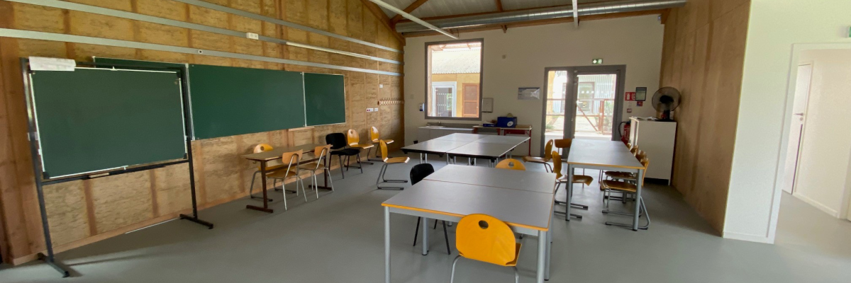 Salle de classe avec tableaux, tables, chaises, évier et porte.