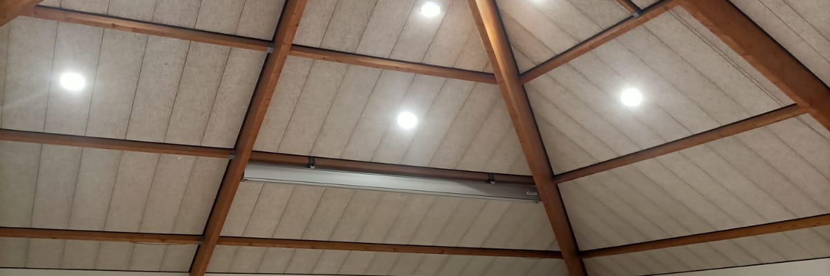 Salle spacieuse avec plafond en bois, tables, chaises et projecteur.