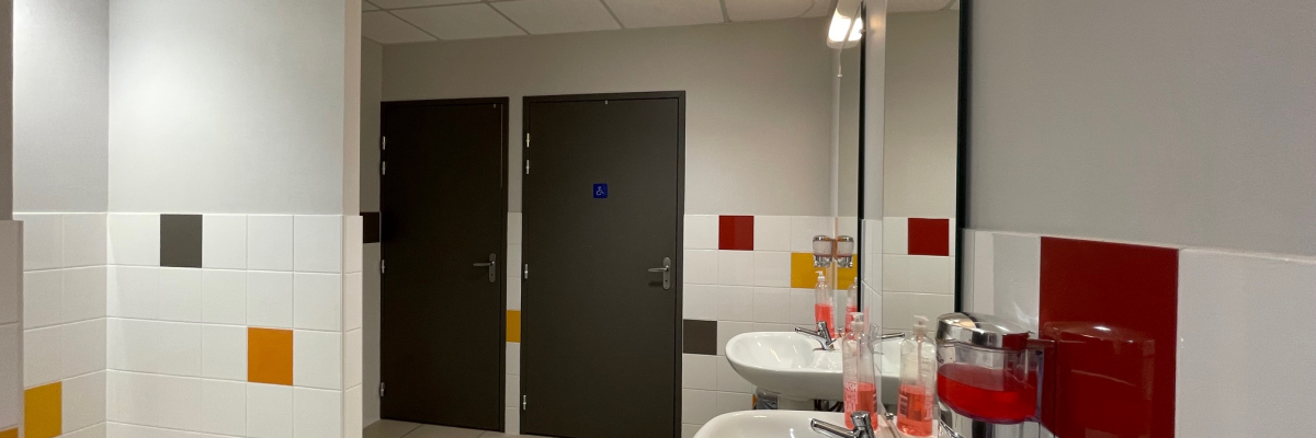 Toilettes avec lavabos, miroirs, savonnettes, sèche-mains et portes en métal.