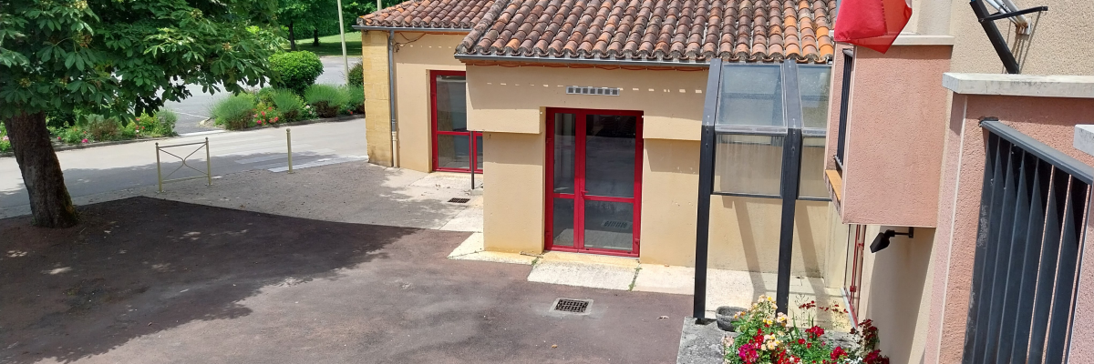 Bâtiment avec toit en tuiles, porte rouge, drapeau français, fleurs, gare, et environnement verdoyant.