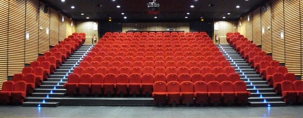 Salle de spectacle avec sièges rouges, scène, éclairages suspendus et parois acoustiques.