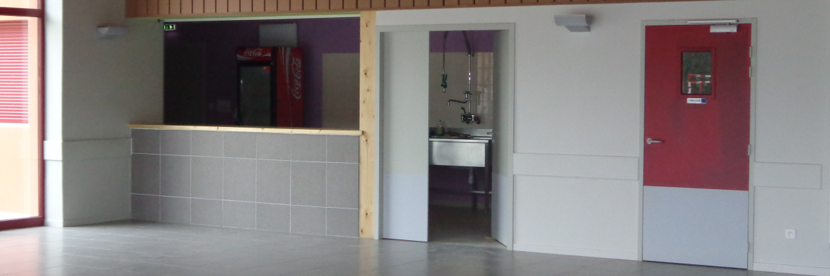 Pièce avec sol carrelé, mur en bois, comptoir, porte blanche, porte rouge et évier visible.