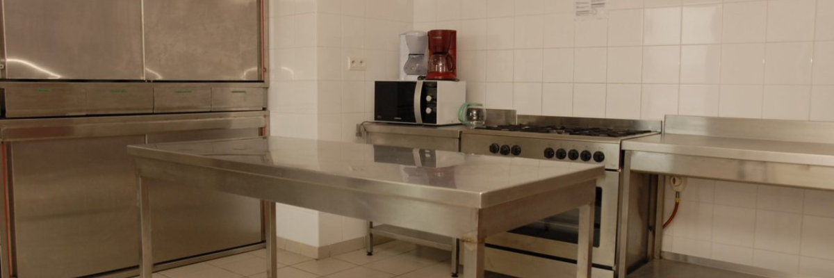 Cuisine avec four, table en acier, micro-ondes, plaque de cuisson et plan de travail.