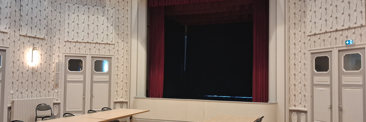 Salle avec tables, chaises, rideau de scène, portes et rampes d'accès.