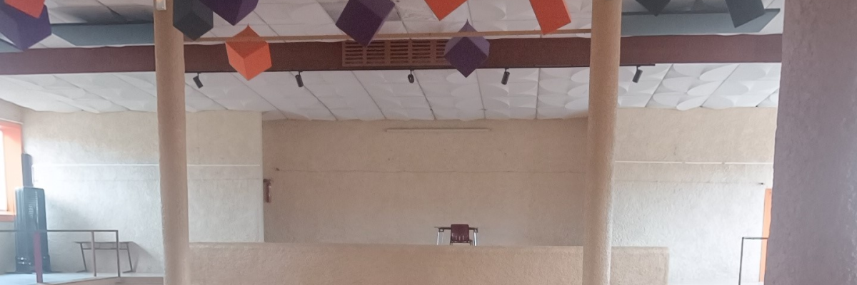 Salle avec colonnes, cubes suspendus, scène, projecteur.