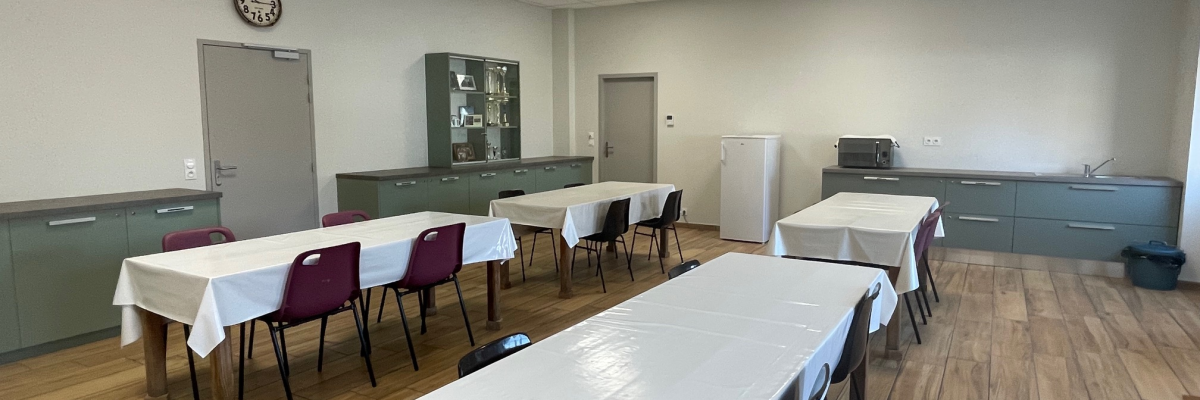 Salle avec tables, chaises, horloge, meubles de rangement et micro-ondes.