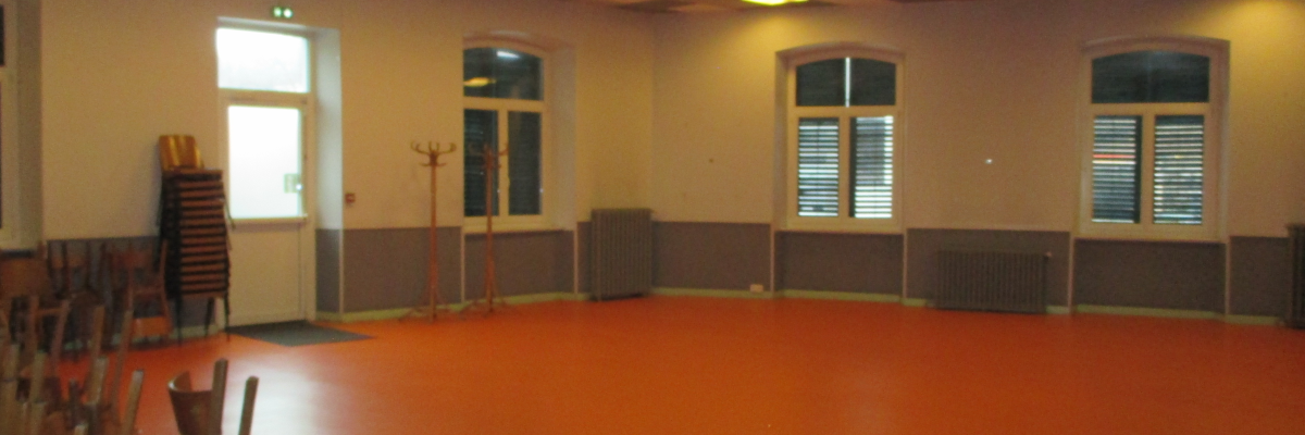 Salle vide avec chaises, sol orange, fenêtres et lumières.