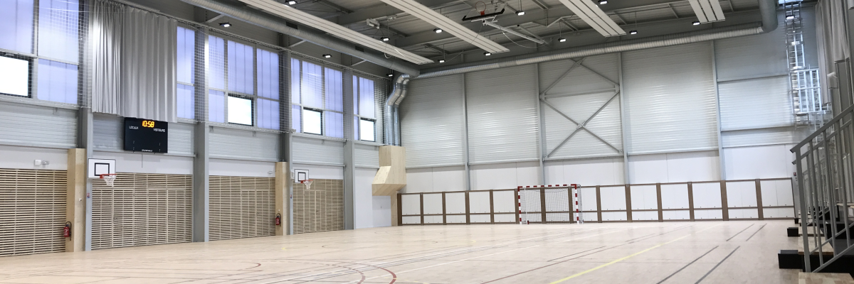 Salle de sport avec parquet, paniers de basket, gradins, panneaux de score et éclairage au plafond.