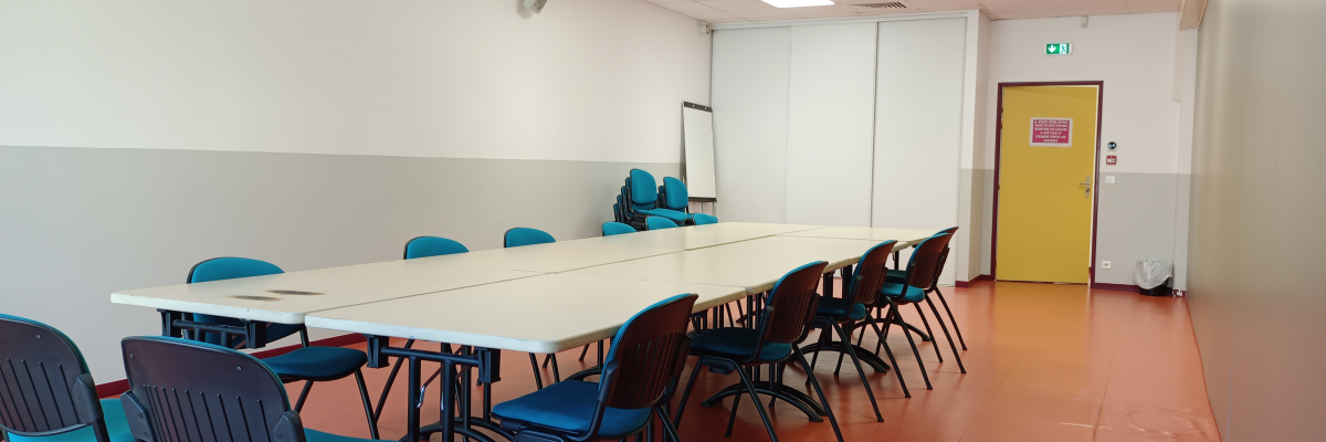 Salle avec table, chaises, tableau blanc, porte jaune et extincteur.