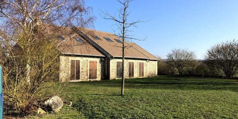 Maison en pierre avec toit en pente, fenêtres rouges, pelouse et arbres.