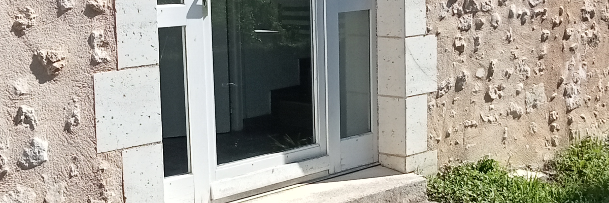 Porte en verre avec cadre de pierre, allée de béton.