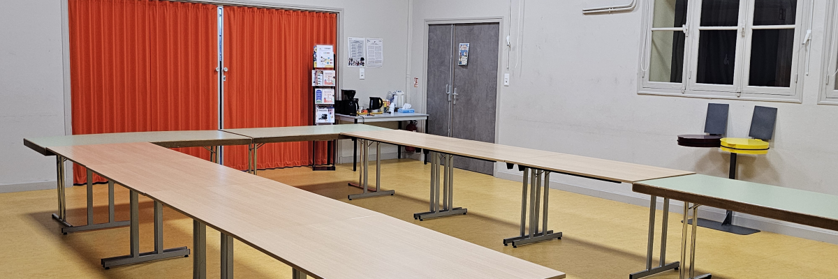 Salle équipée avec tables, chaises, rideau rouge, bureau et fenêtre.