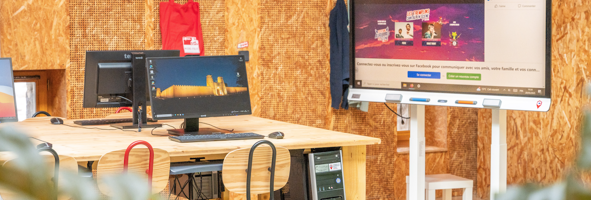 Bureau avec trois écrans, deux claviers, une souris, un sac rouge et un écran mural affichant une vidéo.