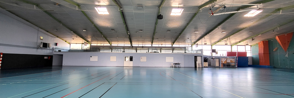 Salle de sport avec paniers de basket, lines de sol, éclairage et murs blancs.