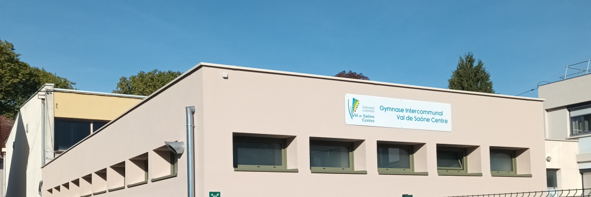 Bâtiment beige avec une enseigne, des fenêtres et une clôture verte.